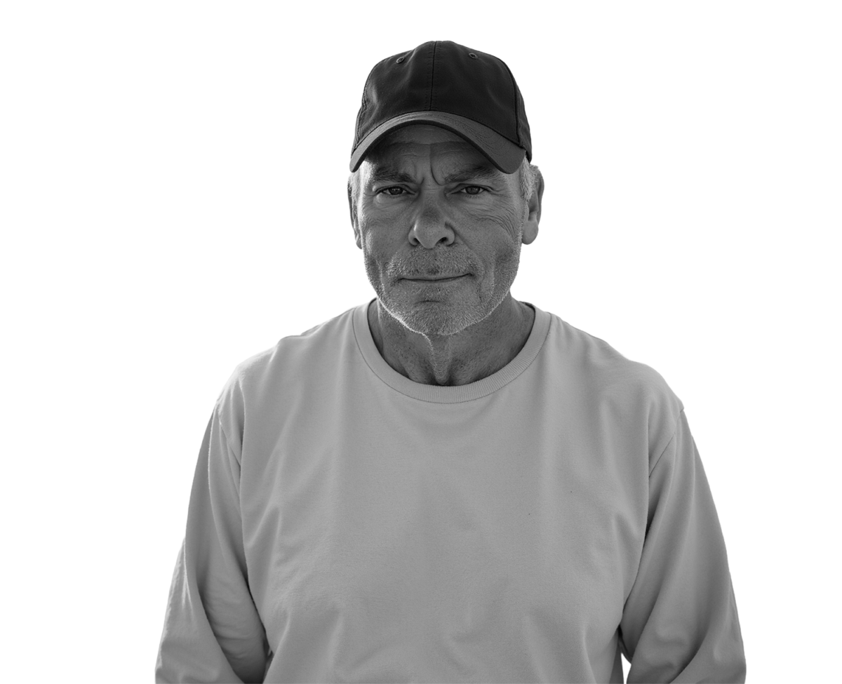 Man in a cap on a beach, black and white portrait with an ocean backdrop.